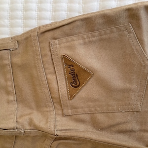 Op de afbeelding: Een beige cargo broek met een bruin leren patch waarop "Candie's" staat.