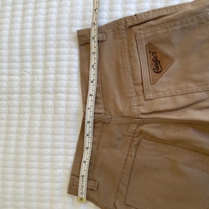 Op de afbeelding: Een bruine corduroy broek met een achterzak die een bruin leren patch heeft met de tekst "Candie's" in witte letters.