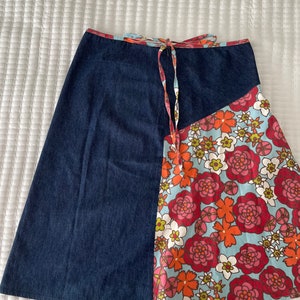 K&ouml;nnte beinhalten: Ein Jeansrock mit einem floralen Print-Panel. Der Rock hat einen Bindeverschluss an der Taille und ist knielang.