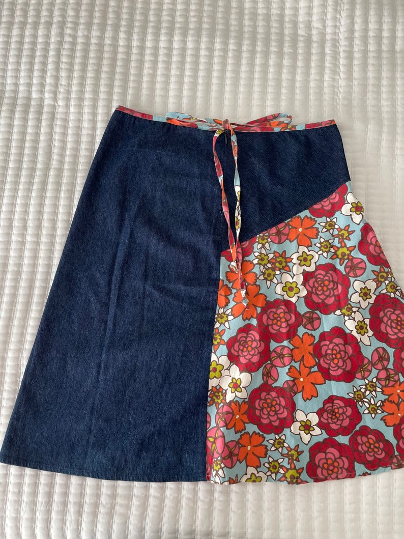K&ouml;nnte beinhalten: Ein Jeansrock mit einem floralen Print-Panel. Der Rock hat einen Bindeverschluss an der Taille und ist knielang.