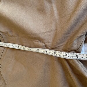 Op de afbeelding: Een bruine broek met een meetlint over de tailleband. Het lint geeft 12 inch aan.