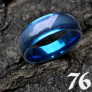 Puede incluir: Un anillo azul con un acabado brillante. El anillo tiene un interior azul brillante y un exterior azul más oscuro. El número "76" está en la esquina inferior derecha de la imagen.