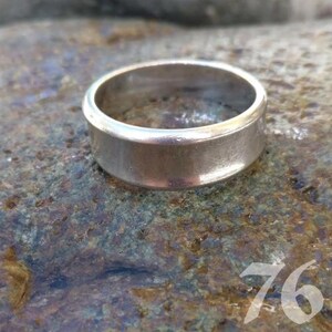 Op de afbeelding: Een gepolijste zilverkleurige metalen ring met een gladde, platte band en een licht verhoogde rand. De ring heeft een eenvoudig, cirkelvormig ontwerp met een reflecterend oppervlak, wat zorgt voor een strakke en uniforme uitstraling over de gehele band.