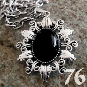 May include: A silver-toned pendant necklace with a large, oval black stone. The pendant has an ornate, filigree design around the stone. The chain is a chunky link style. The number "76" is visible in the bottom right corner.