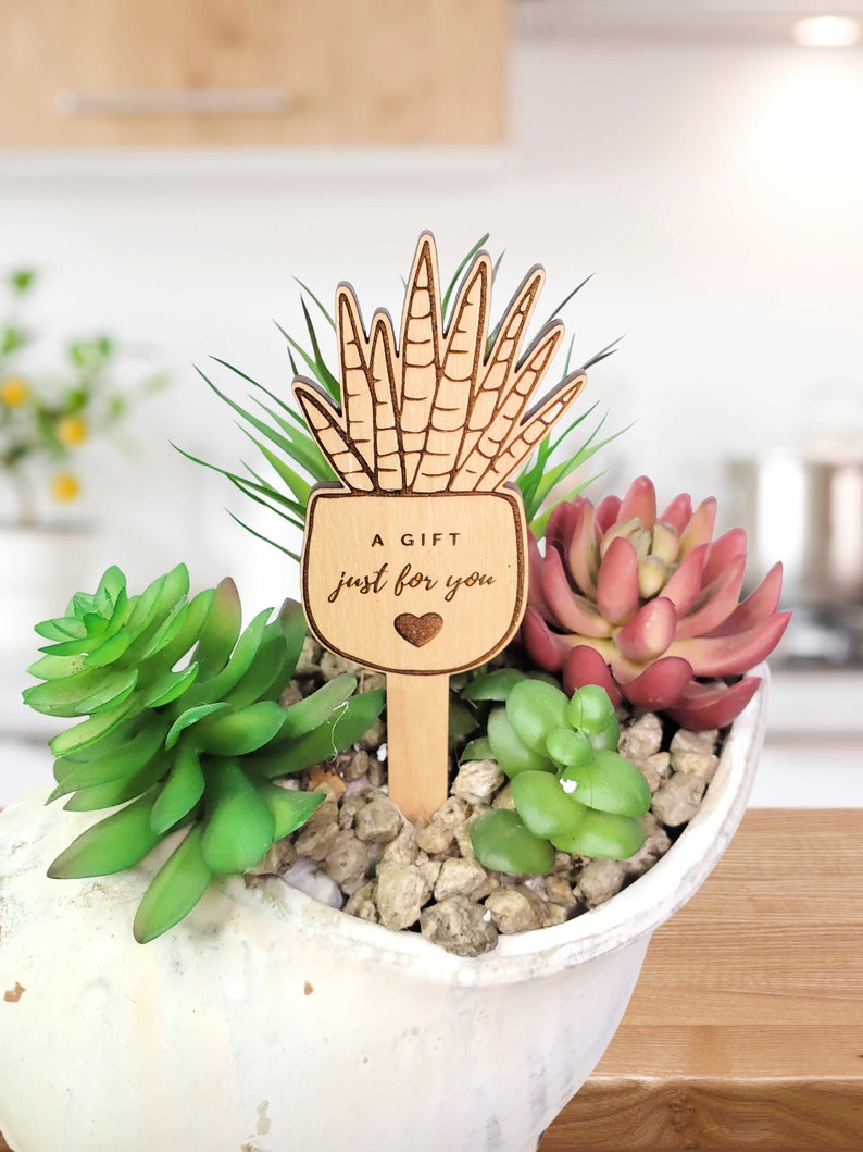 May include: Wooden plant marker with a heart and the text "A gift just for you". The marker is shaped like a potted succulent plant.