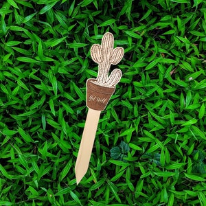May include: Wooden get well soon card with a cactus design. The card is shaped like a stick and has the words "Get Well" written on it.