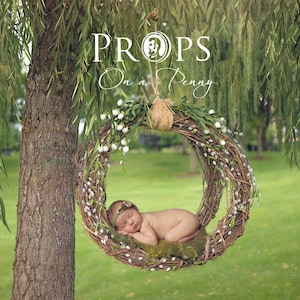 May include: A newborn baby sleeping in a woven wreath hanging from a tree branch. The wreath is decorated with white flowers and green leaves. The text "PROPS On a Penny" is visible above the wreath.