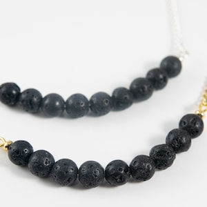 Peut inclure: Deux colliers avec des perles de lave noire. Le collier du haut a une chaîne argentée et le collier du bas a une chaîne dorée.