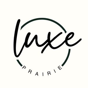 May include: A black circular logo design featuring the word luxe in a large, flowing, handwritten script font centered within the circle, with the word PRAIRIE printed in a smaller, clean, sans-serif capital font along the bottom curve.