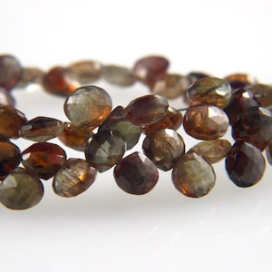 May include: A strand of brown and green faceted gemstone beads. The beads are oval shaped and have a smooth, polished finish.