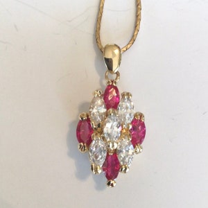 May include: A gold chain necklace with a pendant featuring a cluster of red and white gemstones. The pendant is shaped like a flower with a central white stone surrounded by smaller red and white stones.
