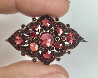 May include: A red garnet brooch with a diamond shape and a pin on the back.