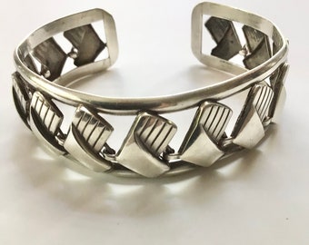 May include: A silver bracelet with a geometric design. The bracelet is made of a series of interlocking silver pieces that form a repeating pattern.