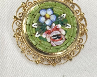 Broche italiano vintage de micromosaico con flores de colores sobre fondo verde y elegante marco de metal chapado en oro.