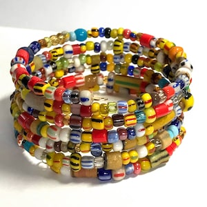 May include: A colorful beaded bracelet with a mix of yellow, red, blue, and white beads. The bracelet is made of multiple strands of beads that are wrapped around each other.