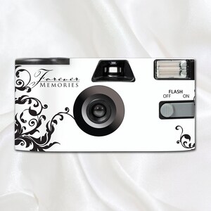 May include: White disposable camera with black floral design and the text "Forever Memories". The camera has a black lens, a flash, and a flash switch with "Flash Off" and "Flash On" labels.
