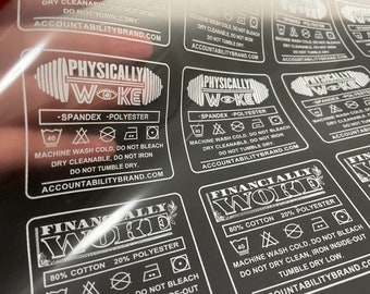 May include: White text on black labels with care instructions for clothing. The labels feature the text "Physically Woke" and "Financially Woke" with a graphic design of a weight and a dollar bill, respectively. The labels also include the text "AccountabilityBrand.com".
