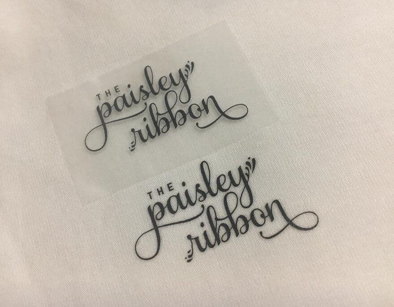 K&ouml;nnte beinhalten: Zwei transparente Etiketten mit schwarzem Text, der in einer kursiven Schrift "The paisley ribbon" lautet.