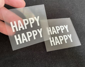 以下が含まれることがあります： 白い文字で「HAPPY」と印刷された透明なプラスチックシートが2枚。シートは重ねられています。