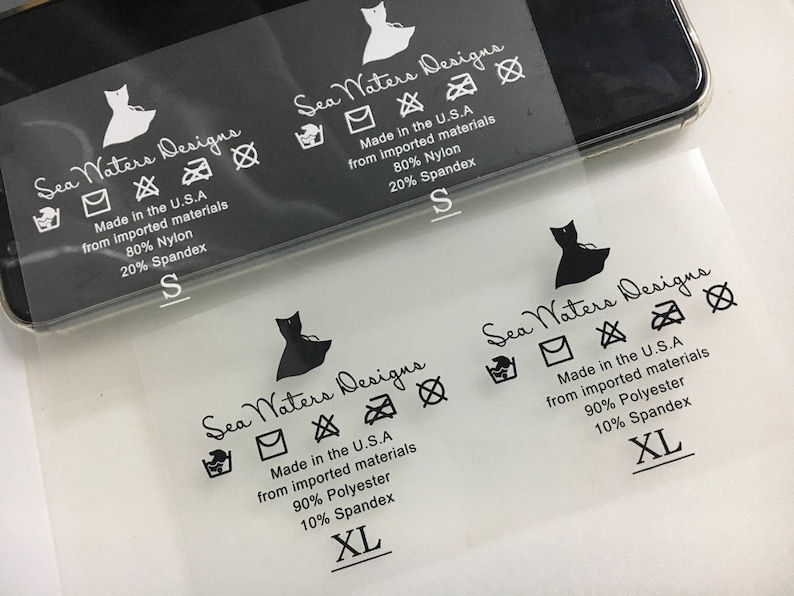 K&ouml;nnte beinhalten: Ein transparentes Kleidungsetikett mit schwarzem Text und Symbolen. Das Etikett lautet "Sea Waters Designs" und enth&auml;lt Pflegehinweise, Gr&ouml;&szlig;e und Stoffzusammensetzung. Die Stoffzusammensetzung ist 80 % Nylon und 20 % Elasthan oder 90 % Polyester und 10 % Elasthan. Die Gr&ouml;&szlig;en sind S und XL.
