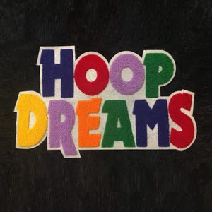 Puede incluir: Un parche colorido con las palabras "HOOP DREAMS" en un estilo universitario. Las letras son de varios colores, incluyendo rojo, morado, verde, amarillo y naranja, sobre un fondo negro.