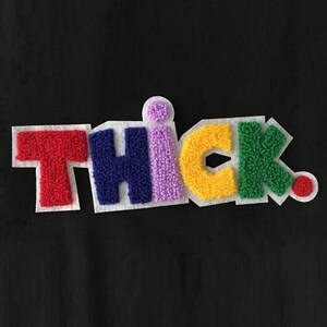 以下が含まれることがあります： 質感のある盛り上がった文字で「THICK」と書かれたカラフルな布製ワッペン。Tは赤、Hは濃い青、Iは薄い紫、Cは黄色、Kは緑色です。Iの上には小さな紫色のドットがあり、Kの後ろには赤いドットが配置されています。