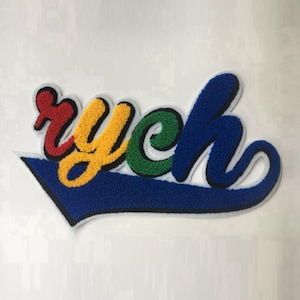 Puede incluir: Un parche bordado colorido con la palabra "ych" en una fuente cursiva juguetona. Las letras son rojas, amarillas, verdes y azules, delineadas en negro, sobre un fondo azul en forma de flecha. El parche tiene una apariencia texturizada y difusa.