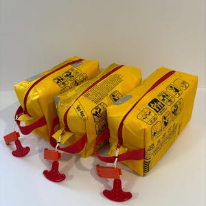 May include: Three yellow inflatable life preservers with red detailing. Each has a red pull handle and a zip closure. The top of each preserver features a red stripe and graphic icons.