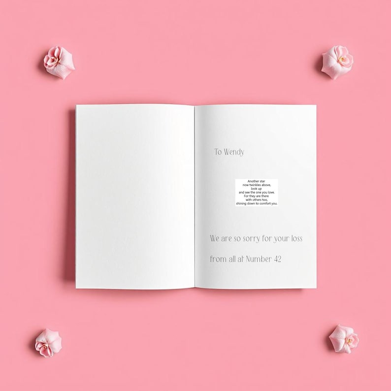 Op de afbeelding: Een open, witte kaart met de tekst "To Wendy" en "We are so sorry for your loss from all at Number 42." Er is ook een kleine, gedrukte boodschap opgenomen. Vier roze bloemen zijn rond de kaart gerangschikt op een roze achtergrond.