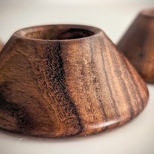 May include: Three wooden coasters with a dark brown wood grain finish. The coasters are shaped like a cone with a rounded top.