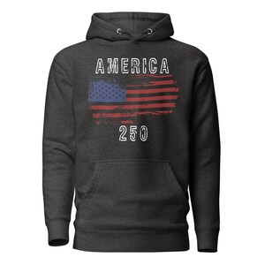 May include: Vintage Black colored hoodie featuring a America 250 with a distressed American Flag. The hoodie has a kangaroo pocket and a drawstring hood. The graphic is detailed with a distressed effect.