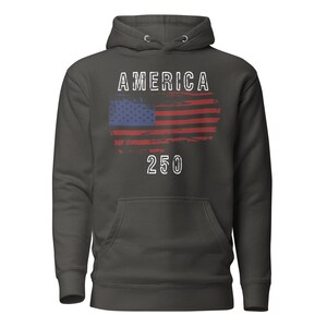 May include: Charcoal Heather colored hoodie featuring a America 250 with a distressed American Flag. The hoodie has a kangaroo pocket and a drawstring hood. The graphic is detailed with a distressed effect.