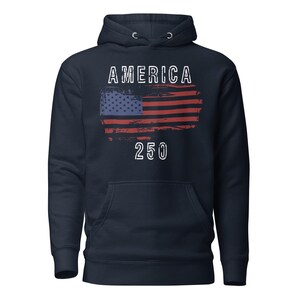 May include: Navy Blue colored hoodie featuring a America 250 with a distressed American Flag. The hoodie has a kangaroo pocket and a drawstring hood. The graphic is detailed with a distressed effect.