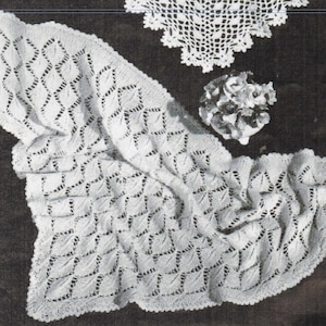 May include: A white, open-weave knitted shawl with a diamond pattern and scalloped edges. The image also shows a small, round doily and a decorative floral element, all in white, against a dark background.