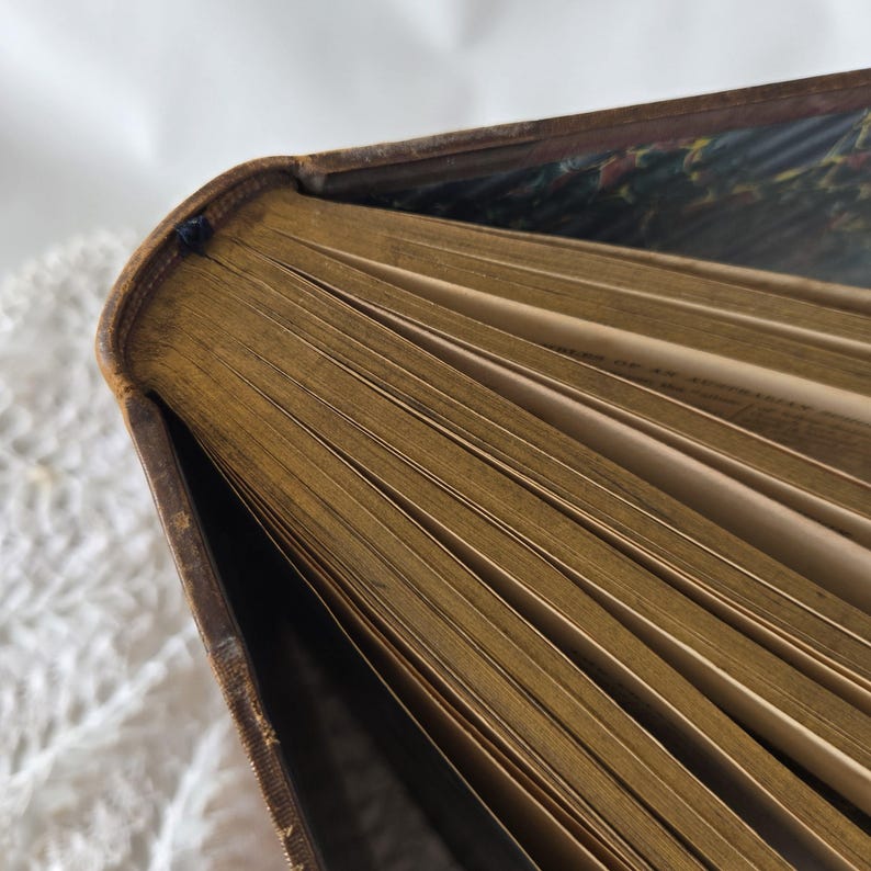 Op de afbeelding: Close-up van een antiek boek met verouderde, vergeelde pagina's. De rug en randen van het boek zijn versleten, met een bruine leren kaft. De pagina's zijn uitgespreid en onthullen de tekst binnenin. De binnenkant van het boek heeft een decoratief patroon.