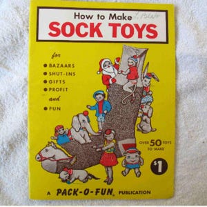 May include: A vintage yellow book cover titled "How to Make Sock Toys." The cover features illustrations of sock toys, including Santa Claus, an elephant, and a dog. The book promises over 50 toys to make.