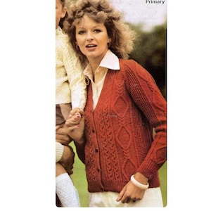 May include: A rust-colored cable-knit cardigan with a V-neck and button closure. The sweater features a diamond pattern and is worn over a white collared shirt. A white bracelet is on the wrist.