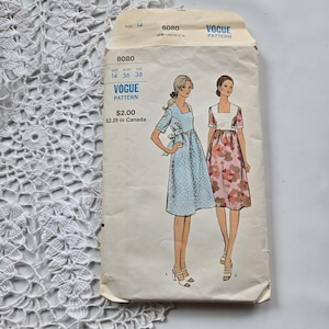 May include: A vintage Vogue sewing pattern envelope, number 8080, size 14, featuring illustrations of two knee-length dresses with square necklines and short sleeves. One dress is light blue with white polka dots, the other has a floral print.