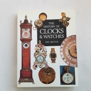 以下が含まれることがあります： エリック・ブルトン著「The History of Clocks & Watches」というタイトルの本。表紙には、背の高い置き時計、人形付きの小さな磁器時計、懐中時計、装飾的な大きな時計の文字盤など、さまざまなアンティーク時計が描かれています。