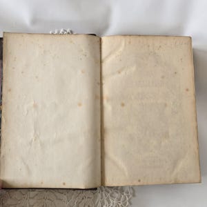 Op de afbeelding: Een open antiek boek met verouderde, cr&egrave;mekleurige pagina's. De pagina's vertonen bruine vlekken en lichte kreukels, wat op leeftijd duidt. De binding is zichtbaar aan de linkerkant en het boek ligt op een wit oppervlak. De tekst "Circa" is zichtbaar in de rechterbovenhoek.