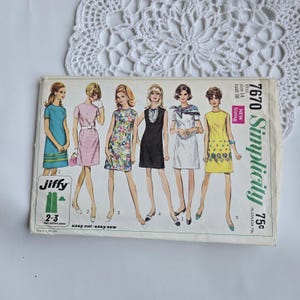 May include: A vintage Simplicity sewing pattern, number 7670, showing illustrations of six dresses. The pattern includes sizing details and the "Jiffy" logo. The cover is aged, with a white lace doily in the background.