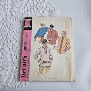 May include: Vintage McCall's sewing pattern for a men's shirt, size medium, chest 96-102 cm. The pattern features illustrations of different shirt styles with decorative trim. The pink and white pattern envelope is visible.