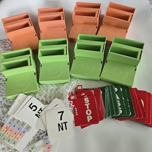 May include: A collection of vintage card game accessories, including orange and green plastic card holders and various playing cards. The card holders have a circular design with a spade symbol. The cards include numbers and the word "STOP".