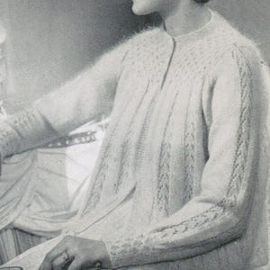 Peut inclure: Un cardigan tricoté vintage de couleur claire, avec un col rond et des manches longues. Le cardigan présente un motif texturé sur le haut de la poitrine et les manches, avec un motif vertical sur le devant. Les manches et les poignets ont une bordure décorative.