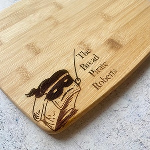 May include: A wooden cutting board with a cartoon illustration of a masked figure and the text "The Bread Pirate Roberts".