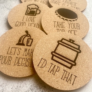 May include: Six round cork coasters with various beer-themed sayings and illustrations. The sayings include "I'm close with my dachs", "My favorite shape is a pound", "I love good head", "Take your top off", "Let's make pour decisions", and "I'd tap that".