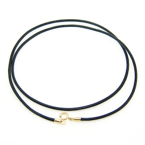May include: A black leather necklace with a gold-colored clasp. The necklace is a simple, elegant design, perfect for everyday wear. The clasp is a small, circular design.