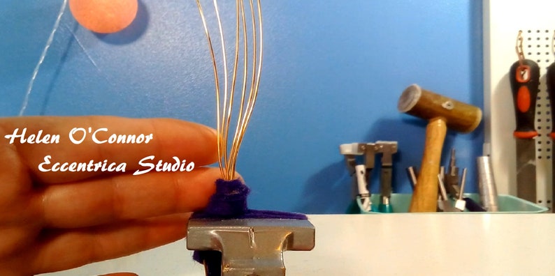 May include: A close-up of a hand holding a metal clamp with multiple gold wires attached to a purple fabric base. The text "Helen O'Connor Eccentrica Studio" is visible in the background.