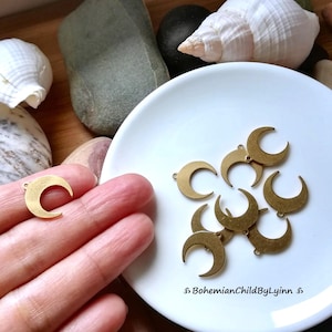 Könnte beinhalten: Nahaufnahme einer weißen Platte mit acht goldenen Halbmond-Anhängern. Die Anhänger haben oben ein Loch zum Anbringen an Schmuck oder andere Bastelarbeiten.