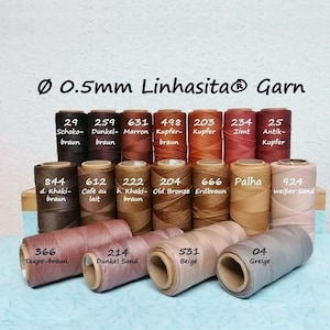 Könnte beinhalten: Eine Sammlung von 0,5 mm Linhasita Garnrollen in verschiedenen Braun-, Beige- und Sandtönen. Jede Rolle ist mit einer Nummer und einem Farbnamen beschriftet, darunter Schoko-braun, Dunkel-braun, Marron, Kupfer-braun, Kupfer, Zimt, Antik-Kupfer und Greige.
